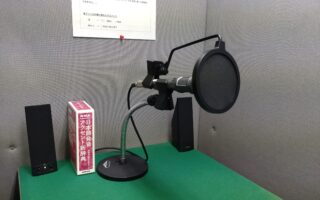 スタジオ内の写真です。 机にマイクとスピーカー、辞書があります。